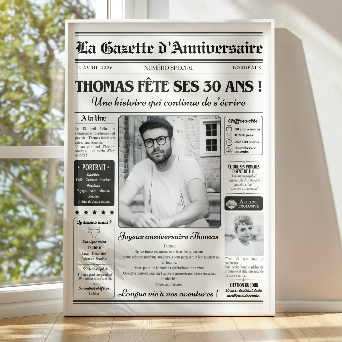 Affiche gazette anniversaire 30 ans avec prénom, portrait et photo d'enfance, présentée dans un cadre blanc près d'une fenêtre.