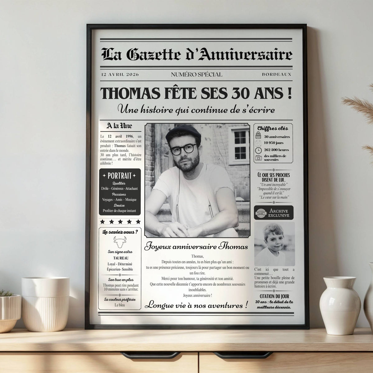 Gazette anniversaire personnalisée pour les 30 ans d'un homme, avec prénom et photos souvenirs, dans un cadre noir sur un meuble.