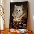 Tableau personnalisé d'une chatte blanche habillée en duchesse, avec bijoux et collerette en dentelle, dans un cadre noir sur un meuble.